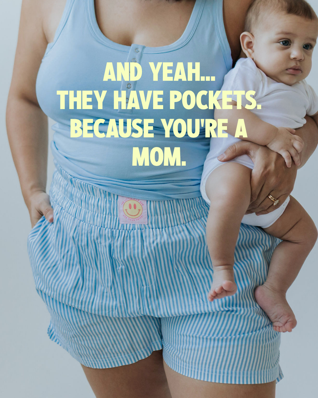 Mom holding her baby with one hand in the real pockets of the Postpartum Boxer Shorts, worn with the matching Postpartum Tank from the little milk bar