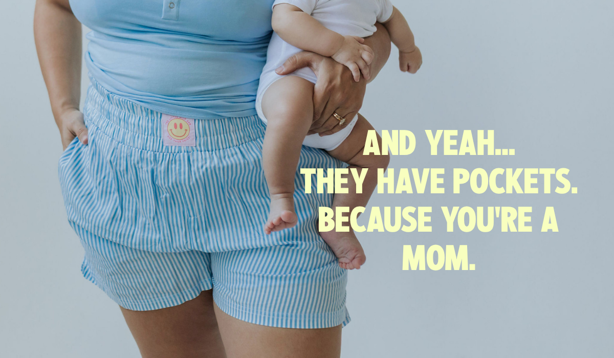 Mom holding her baby with one hand in the real pockets of the Postpartum Boxer Shorts, worn with the matching Postpartum Tank from the little milk bar