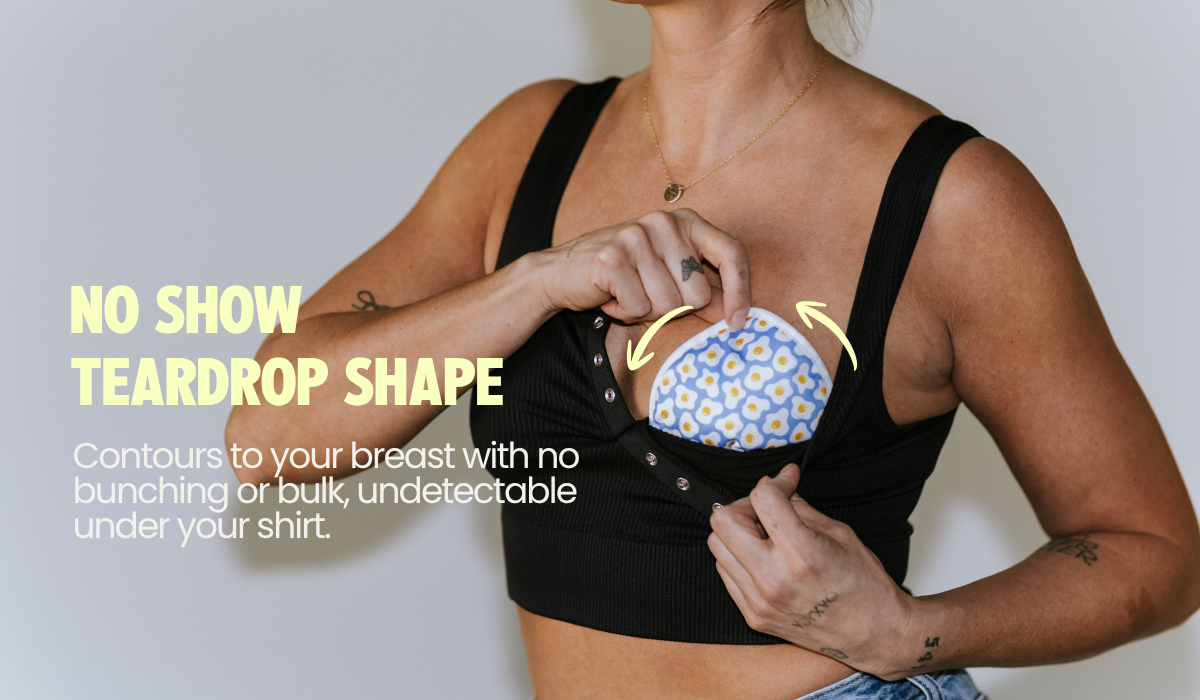 Mom placing a teardrop-shaped reusable nursing pad in her bra, contoured for a discreet no-show fit with no bunching or bulk